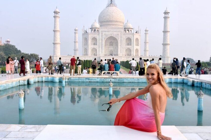 A person in a pink dress standing by a reflective pool with the Taj Mahal in the background. 2