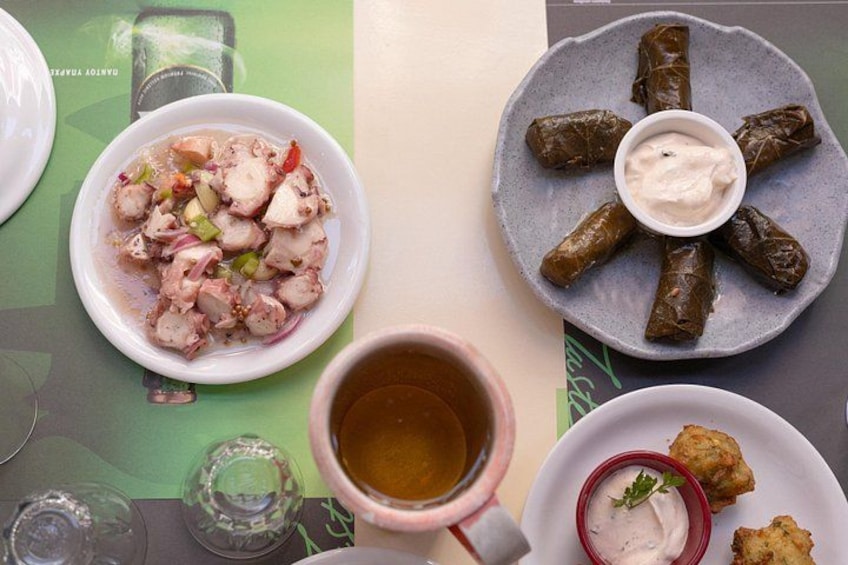 Una mesa con varios platos, incluyendo un plato de hojas de parra rellenas, un bol de carne en rodajas con verduras y una taza de té. 2
