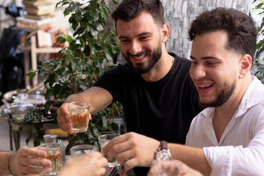 Dos personas brindando con bebidas en una mesa, con una planta al fondo. 1
