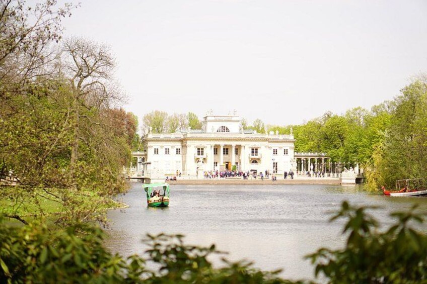 Een rivier met een groene boot, een groot wit gebouw met kolommen, en bomen langs de oevers. 5