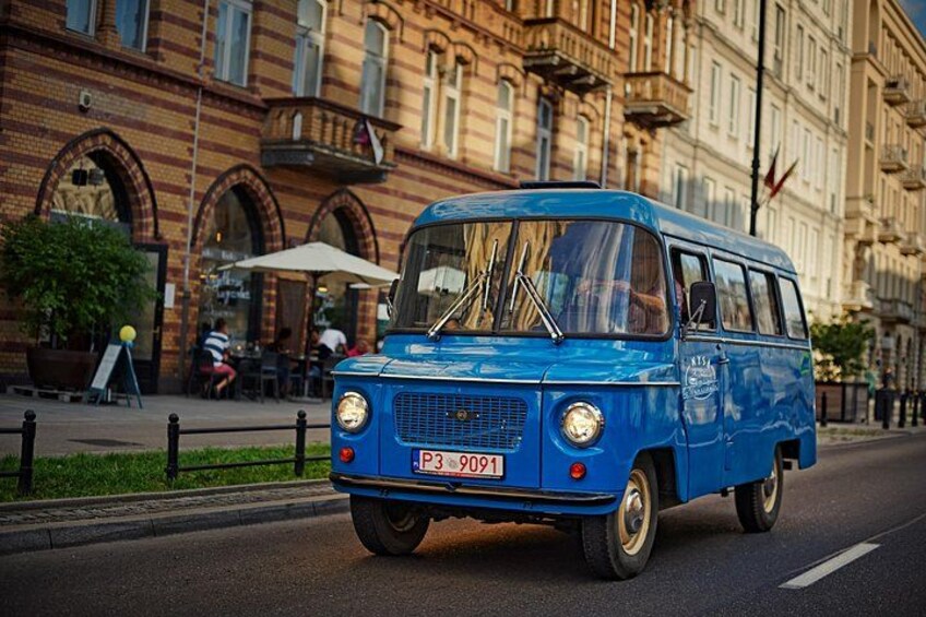A blue vintage van driving on a city street. 2