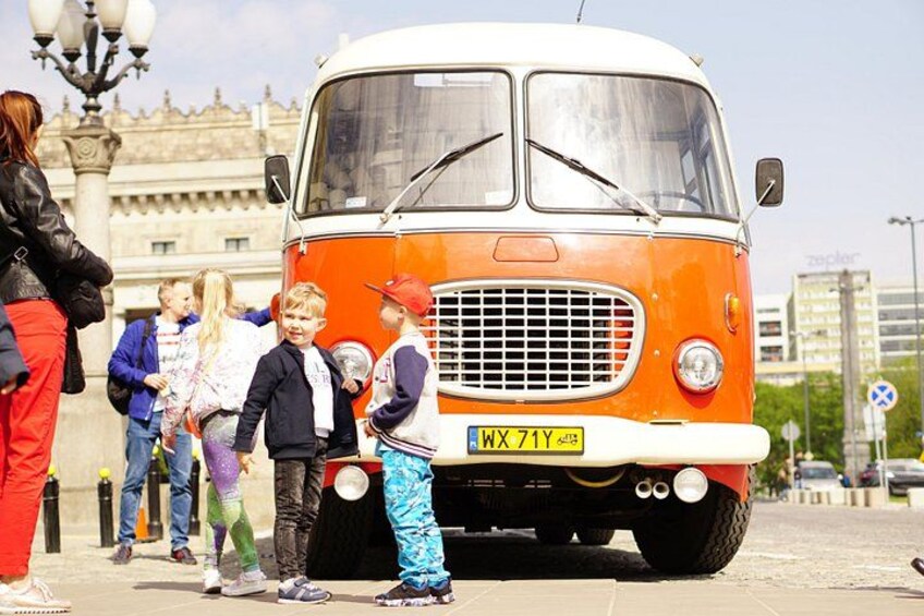 A vintage orange bus with a white roof parked on a cobblestone street. 3