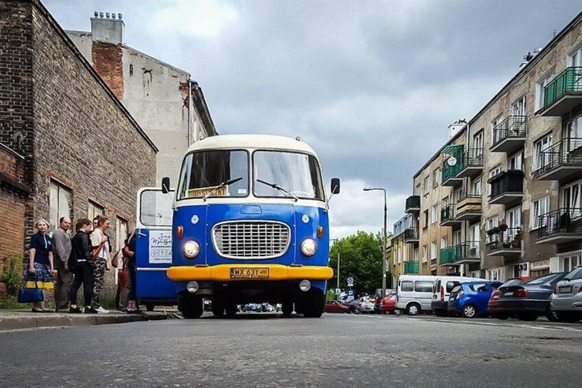 A blue and white vintage bus parked on a street with people standing beside it. 2