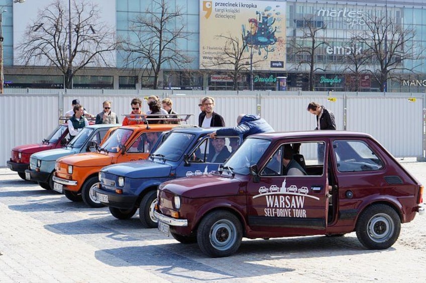 Une rangée de voitures anciennes est garée sur un parking, et des gens se tiennent debout autour. 1