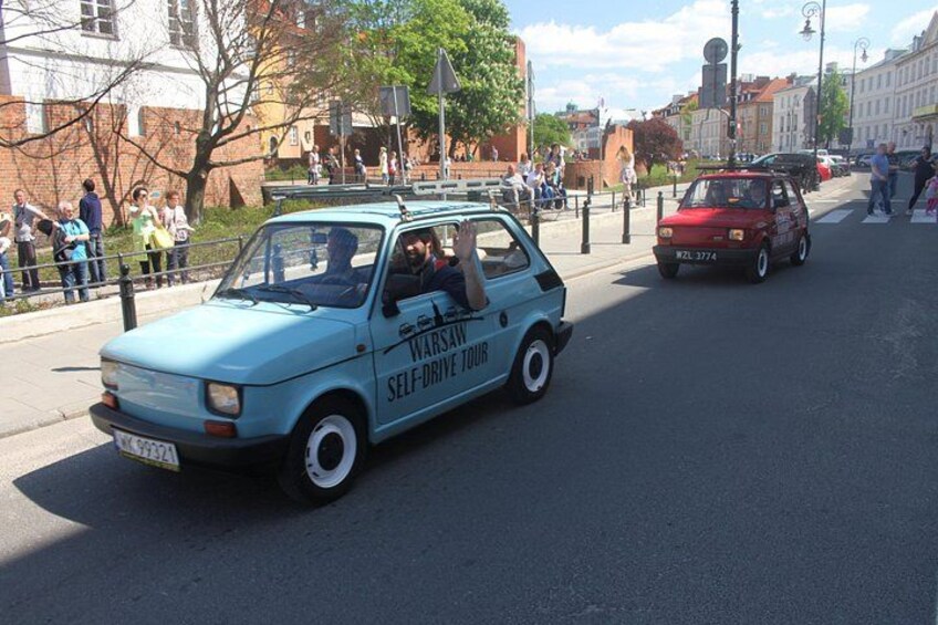 A blue car with 'Warsaw Self-Drive Tour' written on the side driving down a city street. 2