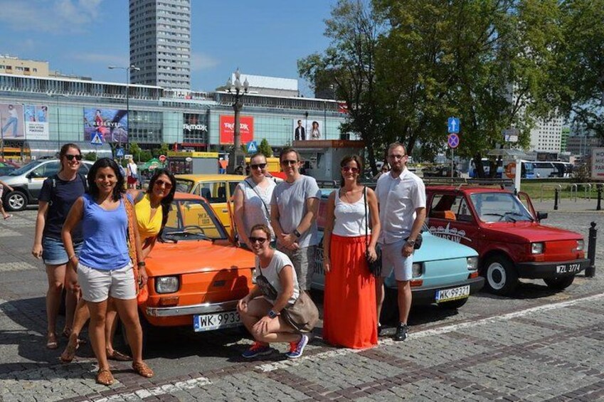 A group of people posing with vintage cars in an urban setting. 5