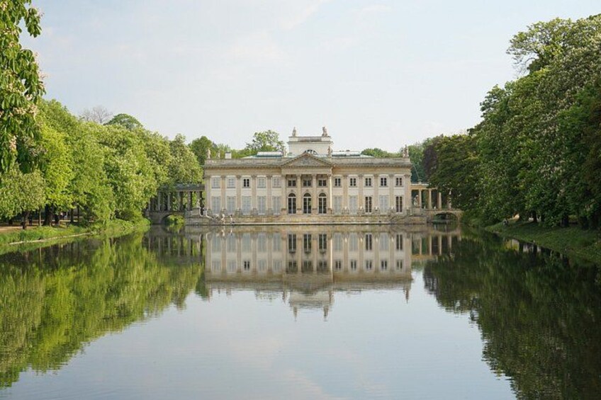 A classical building with a symmetrical facade, a reflecting lake, and lush greenery. 3