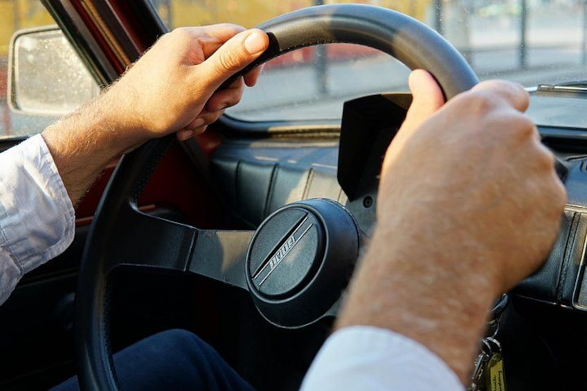 A person driving a car with a steering wheel and dashboard. 3