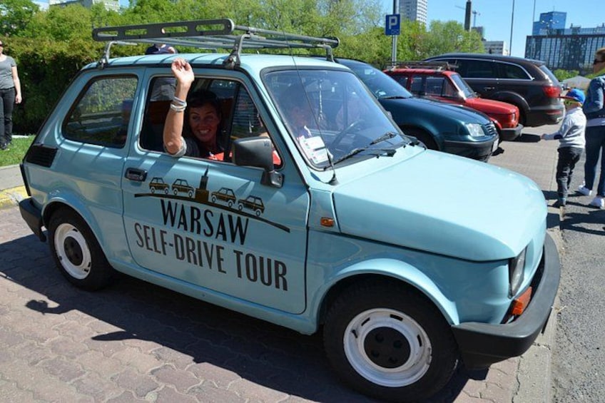 A light blue car with 'Warsaw Self-Drive Tour' written on the side parked in a parking lot. 4