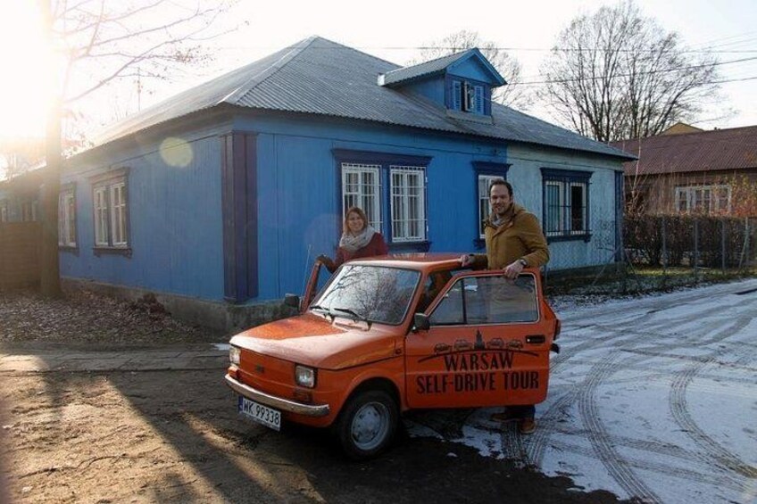 A blue house, a red car with 'Warsaw Self-Drive Tour' written on it, and a person standing next to the car. 3
