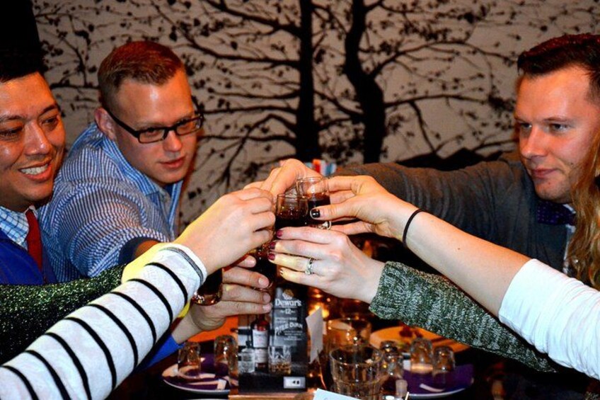 Een groep mensen proost met drankjes aan een tafel vol flessen en glazen. 4