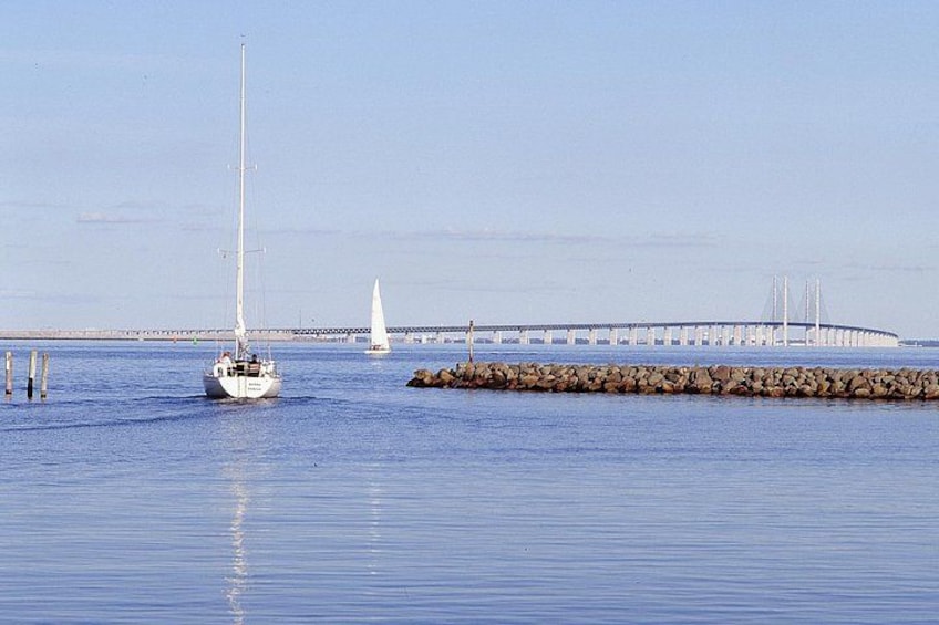 Een zeilboot op rustig water, een verre brug en een rotsachtige zeedijk. 1
