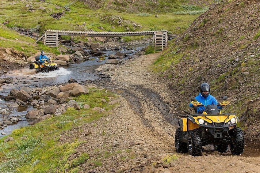 Two off-road vehicles on a dirt path with a bridge in the background. 2