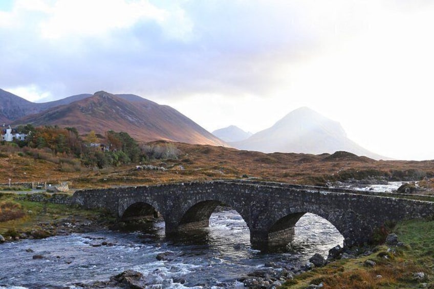 A stone bridge over a river, surrounded by hills and a misty mountain in the background. 2