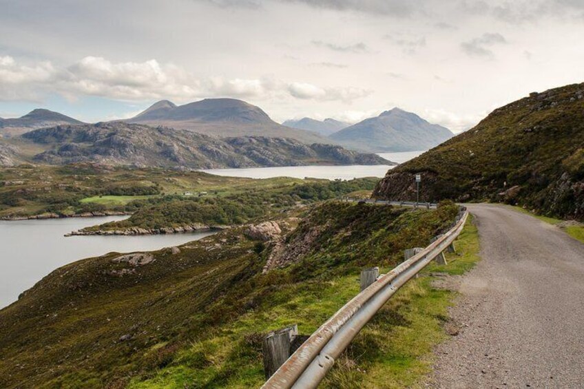 A winding road with a guardrail, surrounded by hills and a lake. 1