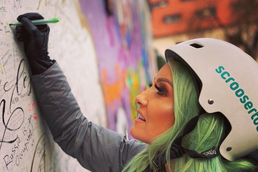 A person with green hair and a helmet, writing on a wall. 2