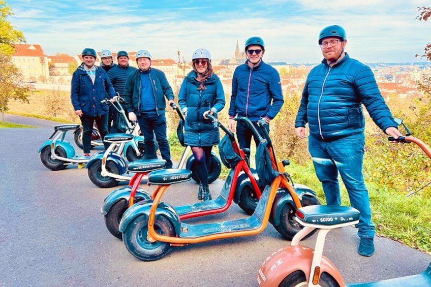 A group of people on electric scooters on a paved path with buildings in the background. 3