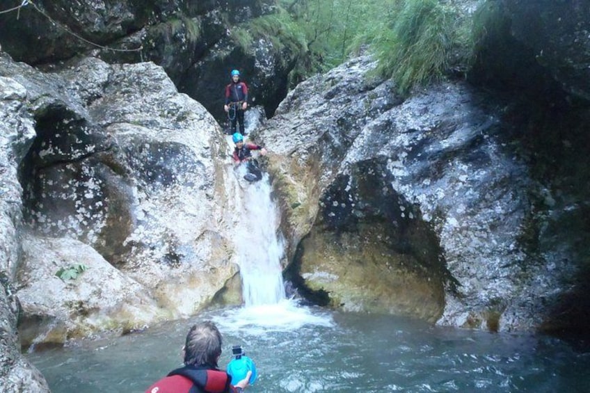 A waterfall in a rocky gorge with two people rappelling down. 1