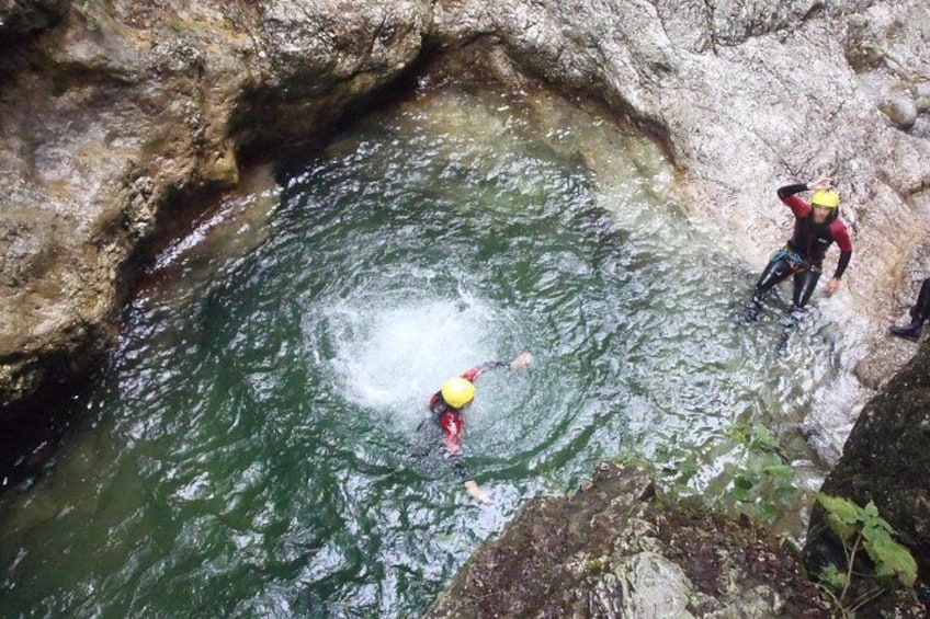 A person in a yellow helmet and red wetsuit swimming in a rocky water body. 3