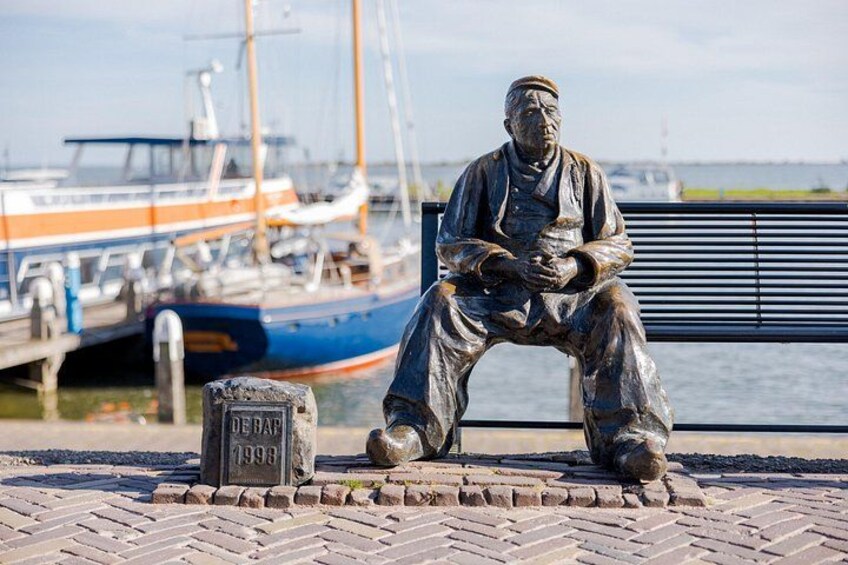 Statua di un uomo seduto con una targa davanti a un molo e barche. 4