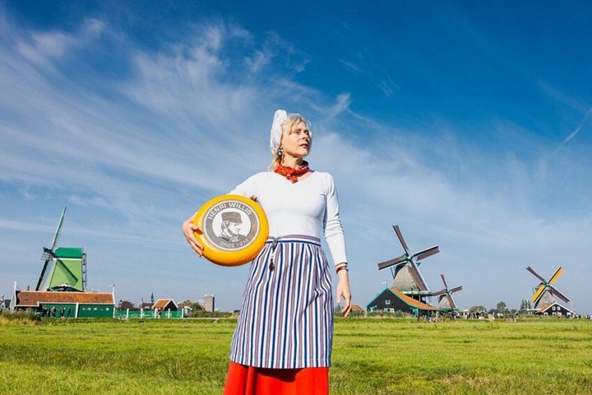 Eine Person in traditioneller Kleidung hält einen Frisbee in einem Feld, im Hintergrund Windmühlen. 4