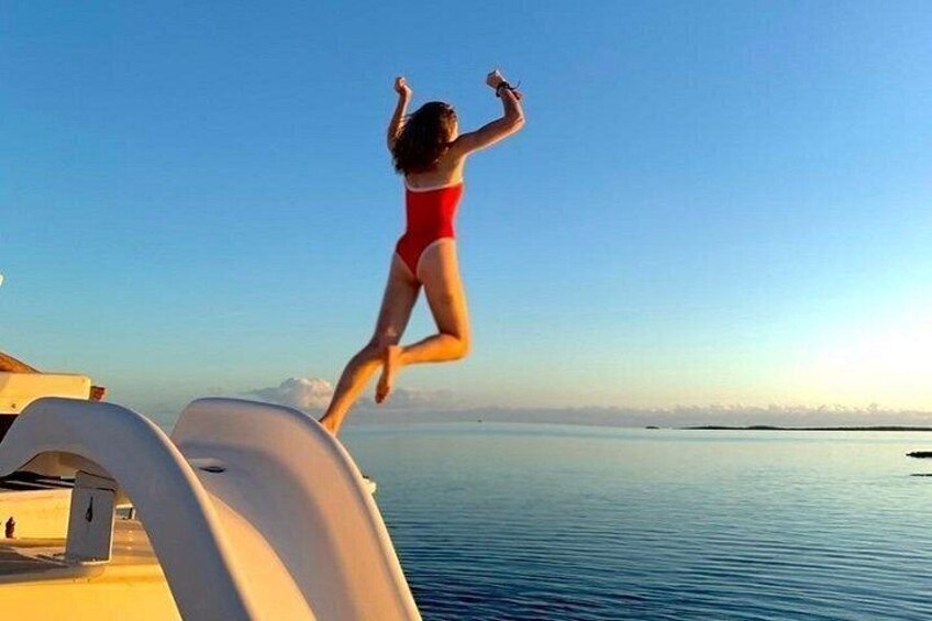 A person in a red swimsuit jumping off a boat into calm water. 5