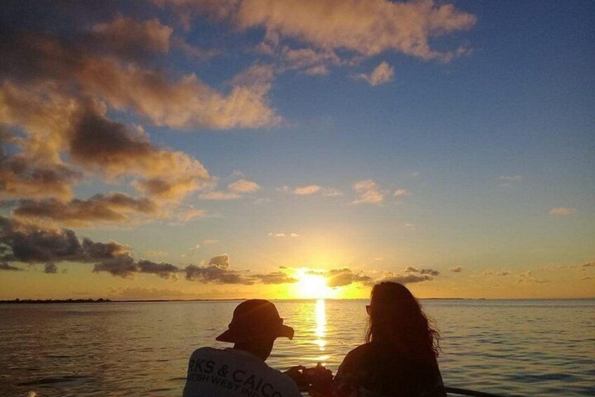 Two people sitting on a boat, facing the sunset over a body of water. 1