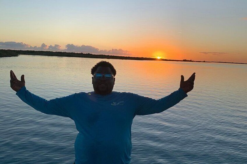 A person standing with arms outstretched in a body of water during sunset. 4