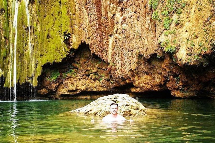 Une personne se trouve dans une piscine naturelle, avec une cascade et des falaises rocheuses en arrière-plan. 2