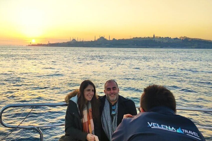Drei Personen in einem Boot vor einer Skyline bei Sonnenuntergang. 1