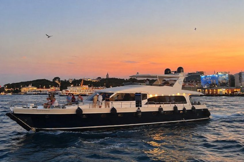 A large boat with people on board, sailing on water with a cityscape in the background during sunset. 2