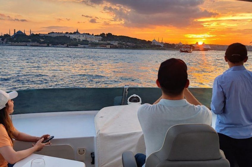 A sunset over a body of water with boats, a cityscape in the background, and people on a boat. 5