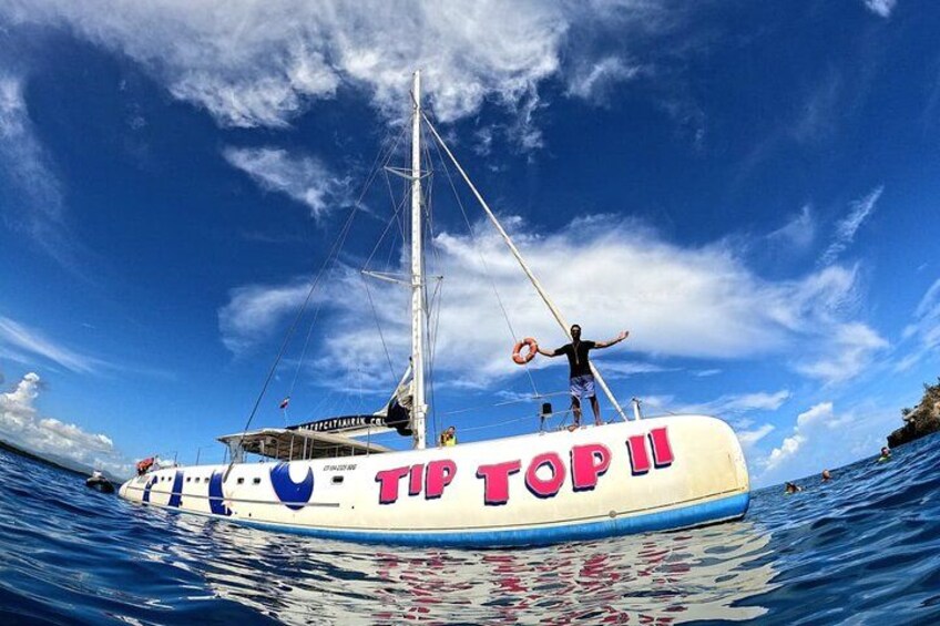 A boat with 'TIP TOP II' written on its side, a person standing on the deck, and the ocean in the background. 1