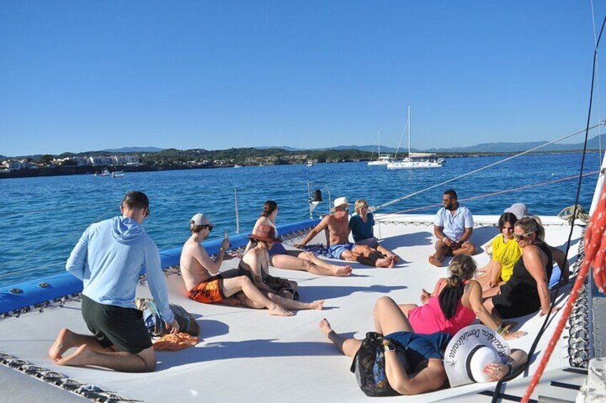 A group of people sitting on a boat in a body of water with a clear sky and distant land. 3
