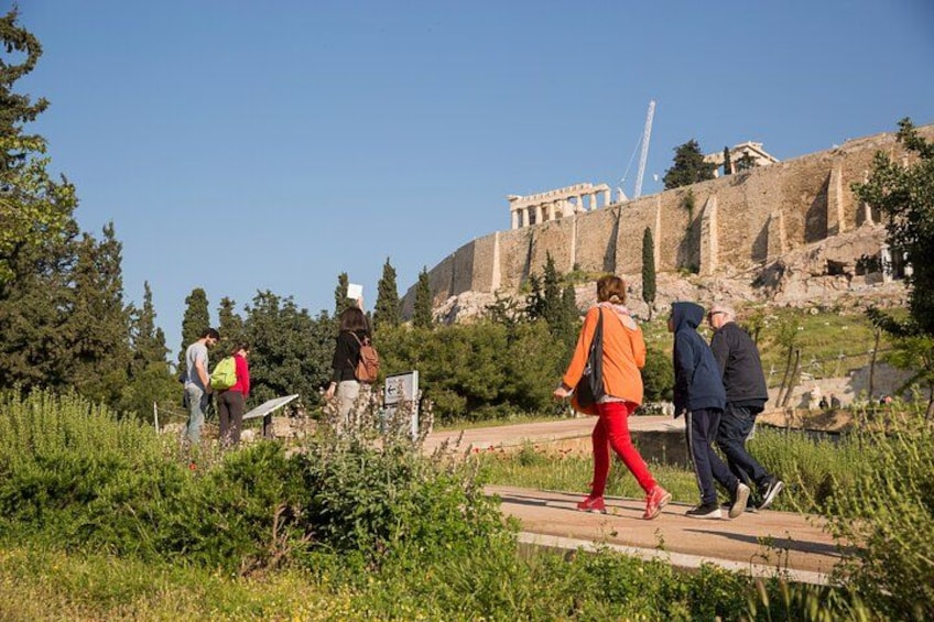 A group of people walking on a path near ancient ruins with columns and a building in the background. 4