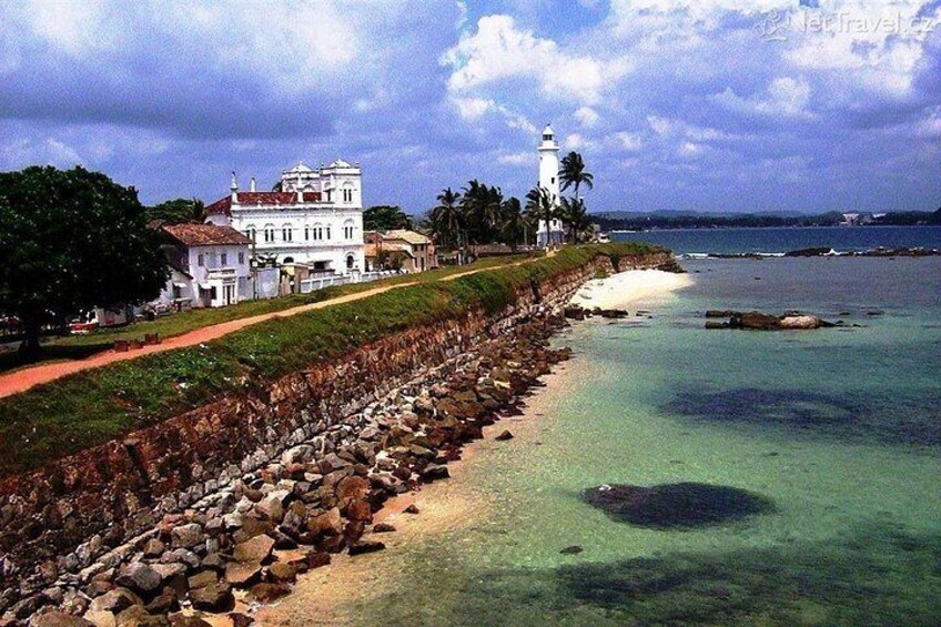 A coastal landscape with a white building, a lighthouse, and a rocky shoreline. 3