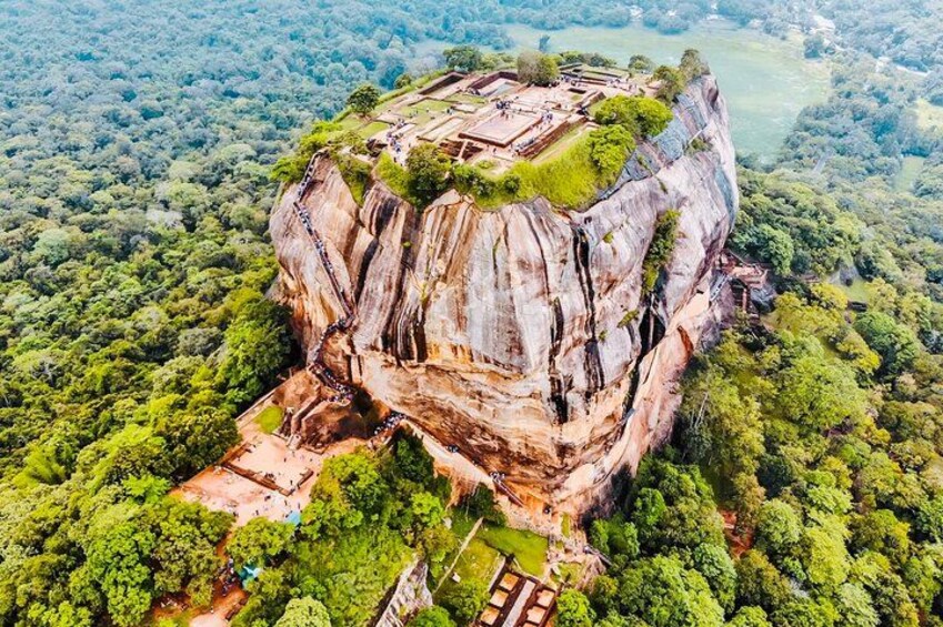 A large rock formation with a temple on top, surrounded by dense forest. 2