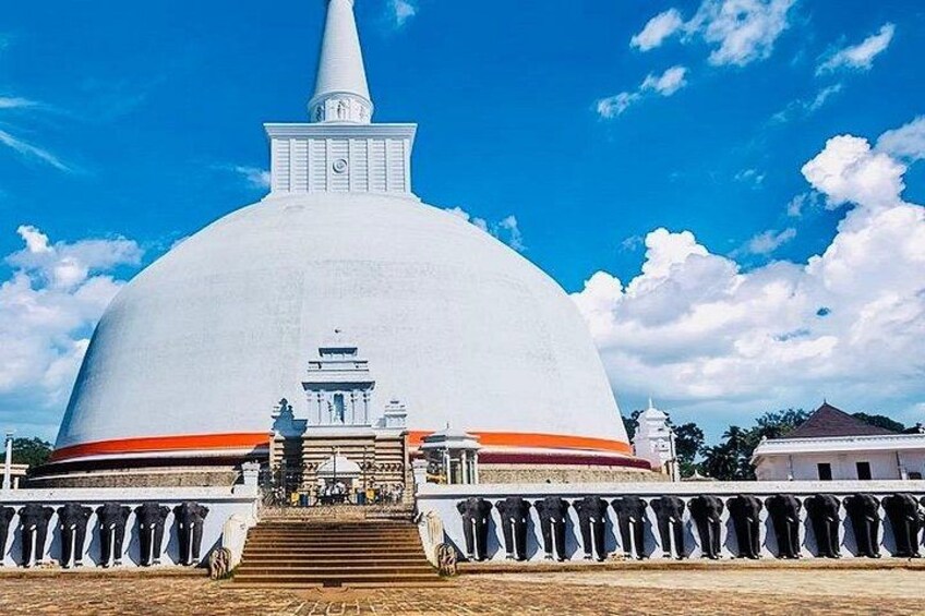 En stor, hvid stupa med en spids spir, omgivet af et gelænder og trapper der fører op til den. 5