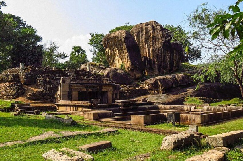 Ancient ruins with stone structures and a large rock formation. 2