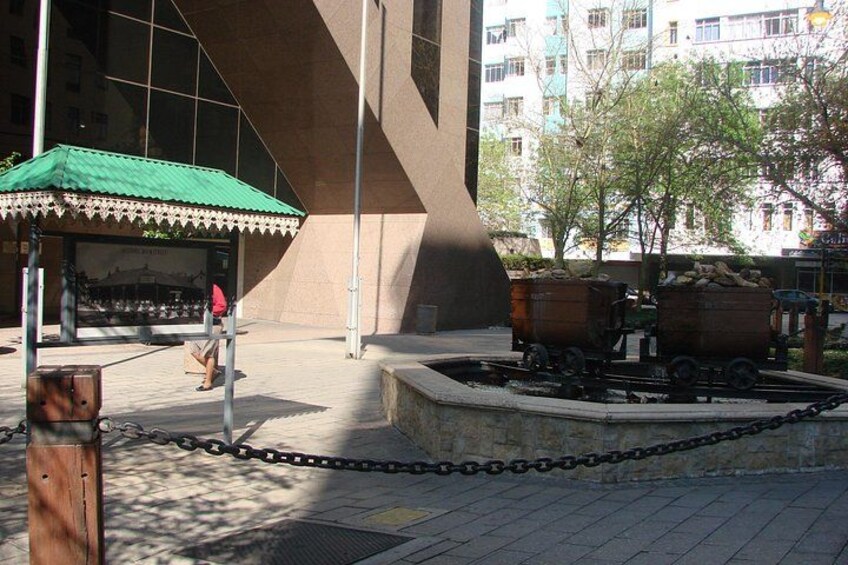 Un espace de repos abrité, délimité par une chaîne, avec une fontaine et un bâtiment moderne en arrière-plan. 5
