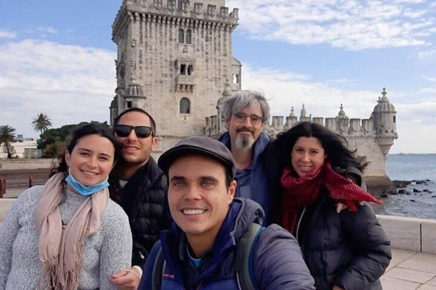 A group of people in front of a historic building with a tower and a body of water in the background. 1