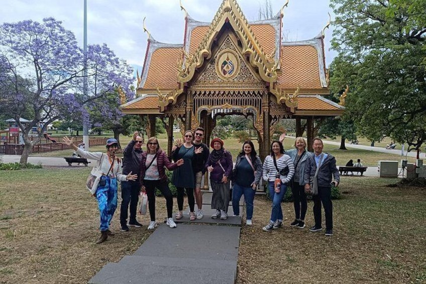 A group of people standing in front of a traditional Thai pavilion with intricate roof design and a central circular window. 4