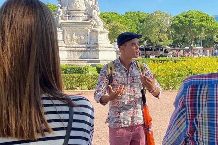 A person gesturing while speaking to a group of people in a park with a statue in the background. 3