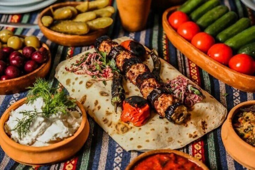 A variety of grilled skewers, flatbreads, and dips on a colorful tablecloth. 2