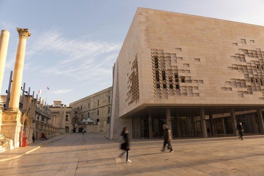 A modern building with a unique facade, a wide open plaza, and classical columns in the background. 5