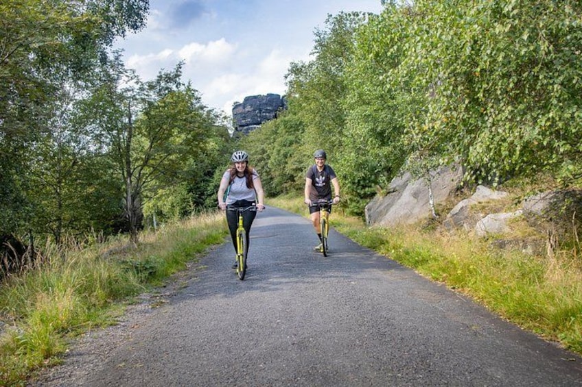 Two cyclists on a paved path surrounded by greenery and rocks. 2