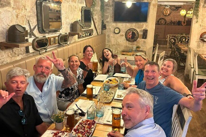 A group of people sitting around a table with food and drinks, in a restaurant with rustic decor. 3