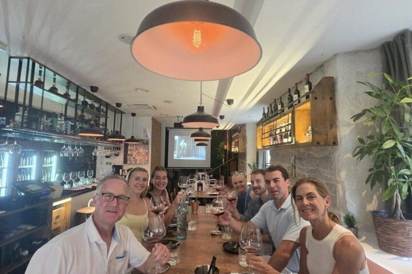 A group of people sitting at a table in a restaurant with wine glasses and bottles. 2