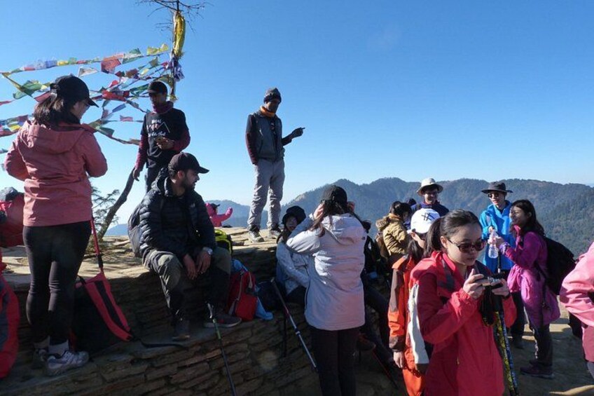 Een groep mensen op een bergkam, sommigen staan en sommigen zitten, met een heldere lucht en bergen in de verte. 3