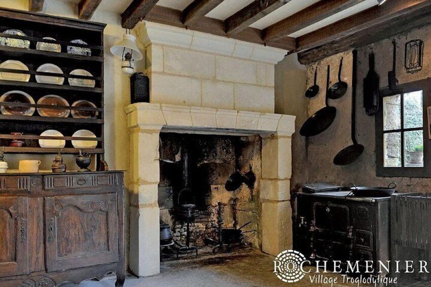 A rustic kitchen with a stone fireplace, hanging pots, and a wooden cabinet with dishes. 2